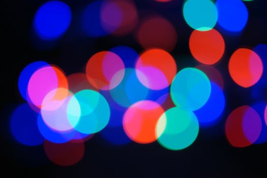 Multi-color blue holiday garland. Garland is blurred. Many big colorful round lights. Fully defocused photo. Blurred background and foreground. Holiday mood. New Year and Christmas is coming.