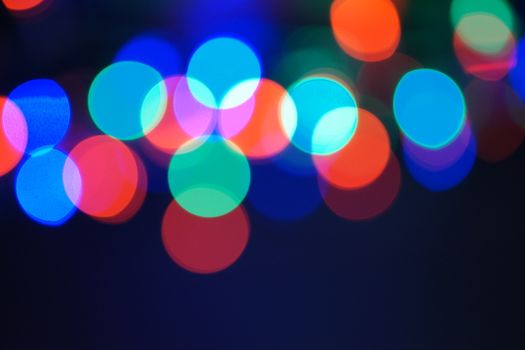 Multi-color blue holiday garland. Garland is blurred. Many big colorful round lights. Fully defocused photo. Blurred background and foreground. Holiday mood. New Year and Christmas is coming.