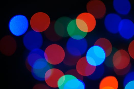 Multi-color blue holiday garland. Garland is blurred. Many big colorful round lights. Fully defocused photo. Blurred background and foreground. Holiday mood. New Year and Christmas is coming.