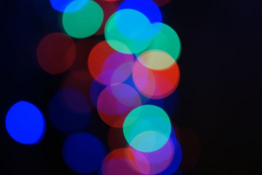 Multi-color blue holiday garland. Garland is blurred. Many big colorful round lights. Fully defocused photo. Blurred background and foreground. Holiday mood. New Year and Christmas is coming.
