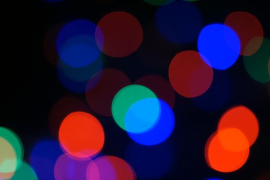 Multi-color blue holiday garland. Garland is blurred. Many big colorful round lights. Fully defocused photo. Blurred background and foreground. Holiday mood. New Year and Christmas is coming.