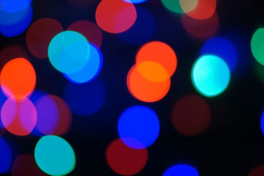 Multi-color blue holiday garland. Garland is blurred. Many big colorful round lights. Fully defocused photo. Blurred background and foreground. Holiday mood. New Year and Christmas is coming.
