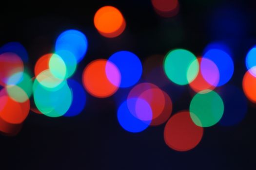 Multi-color blue holiday garland. Garland is blurred. Many big colorful round lights. Fully defocused photo. Blurred background and foreground. Holiday mood. New Year and Christmas is coming.