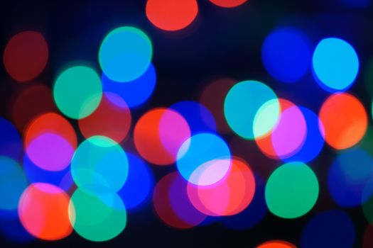 Multi-color blue holiday garland. Garland is blurred. Many big colorful round lights. Fully defocused photo. Blurred background and foreground. Holiday mood. New Year and Christmas is coming.
