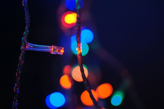 Multi-color blue holiday garland. Garland is blurred. Many big colorful round lights. Fully defocused photo. Blurred background and foreground. Holiday mood. New Year and Christmas is coming.