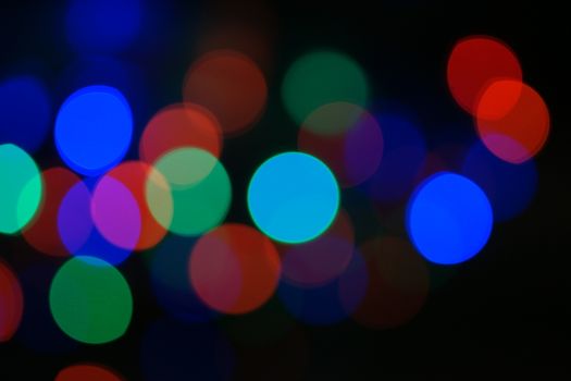 Multi-color blue holiday garland. Garland is blurred. Many big colorful round lights. Fully defocused photo. Blurred background and foreground. Holiday mood. New Year and Christmas is coming.