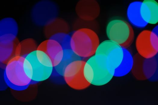 Multi-color blue holiday garland. Garland is blurred. Many big colorful round lights. Fully defocused photo. Blurred background and foreground. Holiday mood. New Year and Christmas is coming.