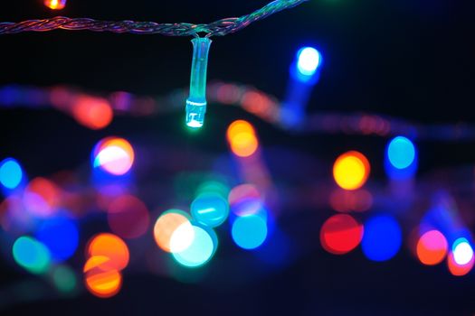 Multi-color blue holiday garland. Garland is blurred. Many big colorful round lights. Fully defocused photo. Blurred background and foreground. Holiday mood. New Year and Christmas is coming.