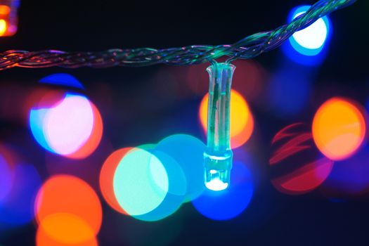 Multi-color blue holiday garland. Garland is blurred. Many big colorful round lights. Fully defocused photo. Blurred background and foreground. Holiday mood. New Year and Christmas is coming.