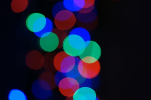 Multi-color blue holiday garland. Garland is blurred. Many big colorful round lights. Fully defocused photo. Blurred background and foreground. Holiday mood. New Year and Christmas is coming.