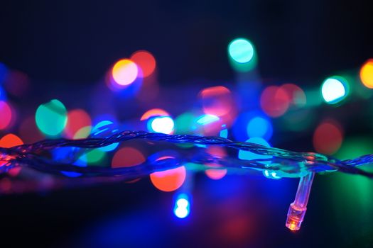 Multi-color blue holiday garland. Garland is blurred. Many big colorful round lights. Fully defocused photo. Blurred background and foreground. Holiday mood. New Year and Christmas is coming.