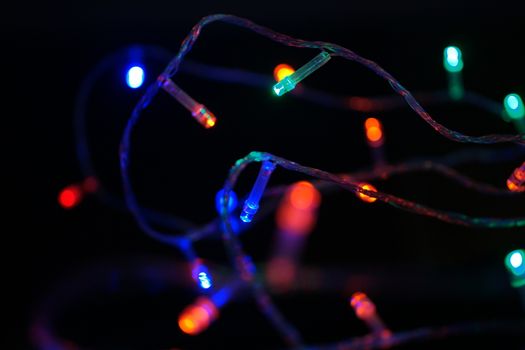 Multi-color blue holiday garland. Garland is blurred. Many big colorful round lights. Fully defocused photo. Blurred background and foreground. Holiday mood. New Year and Christmas is coming.