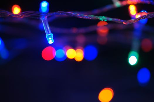 Multi-color blue holiday garland. Garland is blurred. Many big colorful round lights. Fully defocused photo. Blurred background and foreground. Holiday mood. New Year and Christmas is coming.