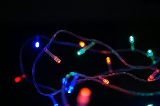 Multi-color blue holiday garland. Garland is blurred. Many big colorful round lights. Fully defocused photo. Blurred background and foreground. Holiday mood. New Year and Christmas is coming.