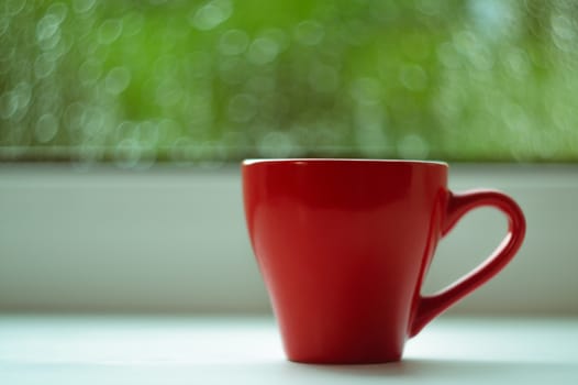 The red espresso cup on white windowsill. On background window and rain. Cup located at right of frame.