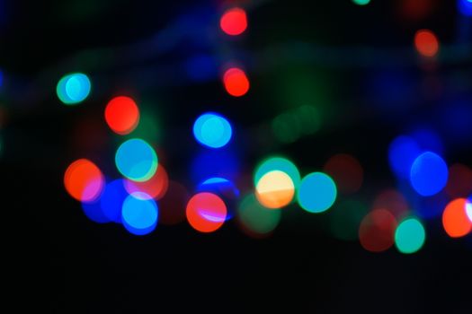 Multi-color blue holiday garland. Garland is blurred. Many big colorful round lights. Fully defocused photo. Blurred background and foreground. Holiday mood. New Year and Christmas is coming.