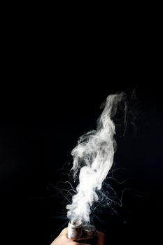 Male hand holds vape without atomiser. Column of vape clouds splash from coil on black background. Fog is white. Stock isolated white smoke with spray boiling glycerine.