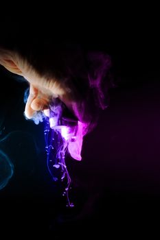 Male hand holds vape upside down. Vape clouds splash from coil on black background. Fog is two-colour blue and purple. Stock isolated dual color smoke with spray boiling glycerine.