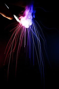 Male hand holds vape upside down. Vape clouds splash from coil on black background. Fog is blue and red colour. Stock isolated smoke with spray boiling glycerine.