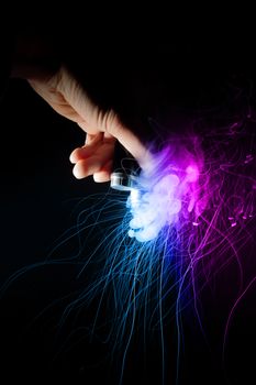 Male hand holds vape upside down. Vape clouds splash from coil on black background. Fog is two-colour blue and purple. Stock isolated dual color smoke with spray boiling glycerine.