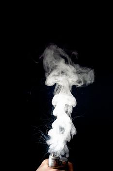 Male hand holds vape without atomiser. Column of vape clouds splash from coil on black background. Fog is white. Stock isolated white smoke with spray boiling glycerine.