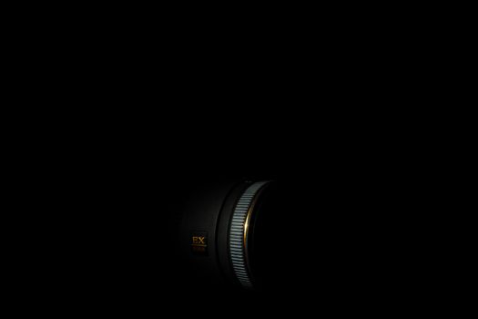 Ukraine; Kyiv; 20.02.2019 Sigma 50mm f1:2,8 DG EX Macro lens. Underexposed photo of DSLR camera lens on black background. Stock photo isolated. Low light photo and large depth of field.