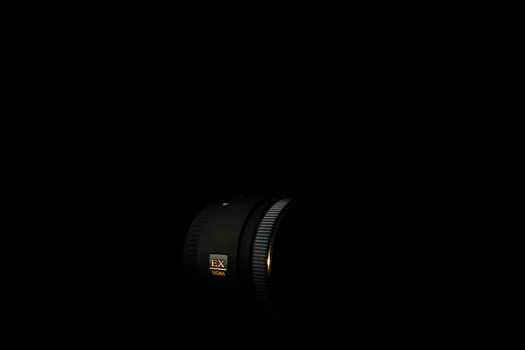 Ukraine; Kyiv; 20.02.2019 Sigma 50mm f1:2,8 DG EX Macro lens. Underexposed photo of DSLR camera lens on black background. Stock photo isolated. Low light photo and large depth of field.