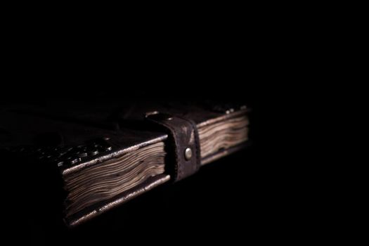 Handmade old leather cover notebook. Charred sheets and leather clasp isolated on black background. Underexposed stock photo.