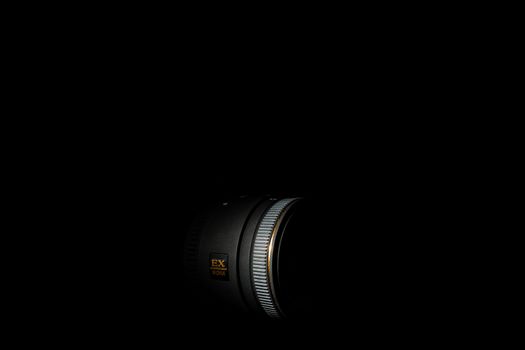 Ukraine; Kyiv; 20.02.2019 Sigma 50mm f1:2,8 DG EX Macro lens. Underexposed photo of DSLR camera lens on black background. Stock photo isolated. Low light photo and large depth of field.