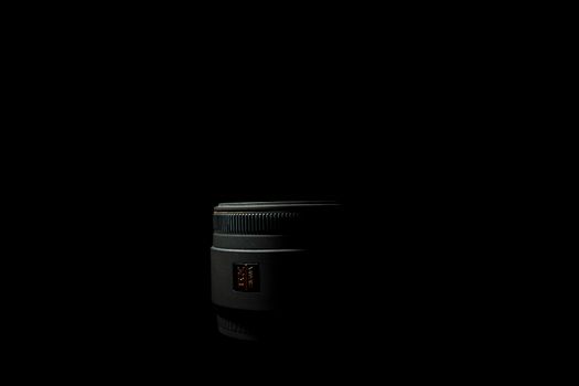 Ukraine; Kyiv; 20.02.2019 Sigma 50mm f1:2,8 DG EX Macro lens. Underexposed photo of DSLR camera lens lying on black background. Stock photo isolated. Low light photo and large depth of field.
