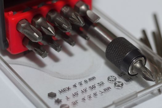 Bits holder in box and many tool bits on white background. Close-up view. Red element in plastic box.