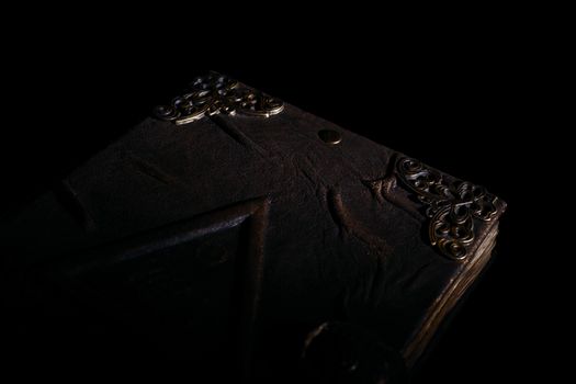 Low light old handmade leather cover notebook. Old leather cover and charred sheets isolated on black background. Underexposed stock photo.