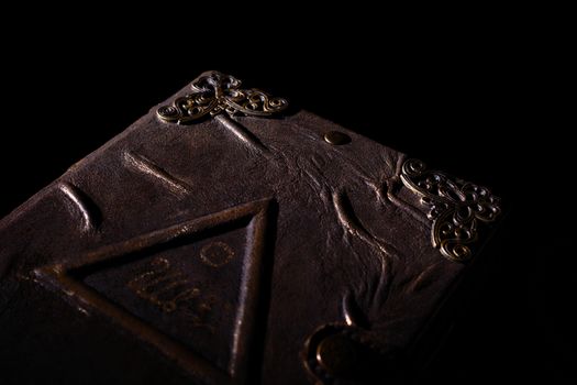 Low light handmade old leather cover notebook. Charred sheets and cover isolated on black background. Underexposed stock photo.