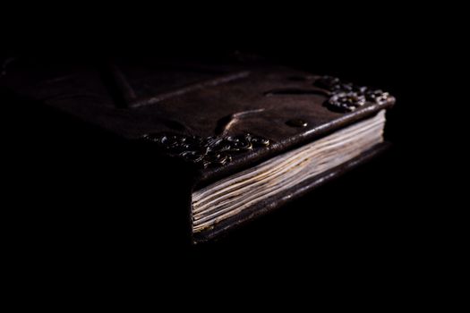 Low light old handmade leather cover notebook. Old leather cover and charred sheets isolated on black background. Underexposed stock photo.