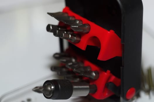 Bits holder in box and many tool bits on white background. Close-up view. Red element in plastic box.