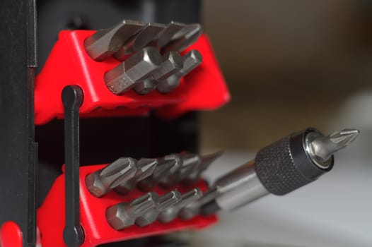 Bits holder in box and many tool bits on white background. Close-up view. Red element in plastic box.