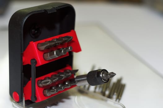Bits holder in box and many tool bits on white background. Close-up view. Red element in plastic box.