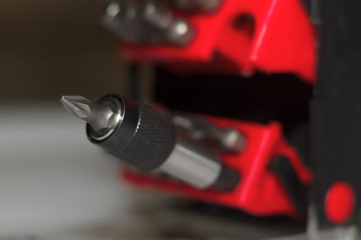 Bits holder in box and many tool bits on white background. Close-up view. Red element in plastic box.