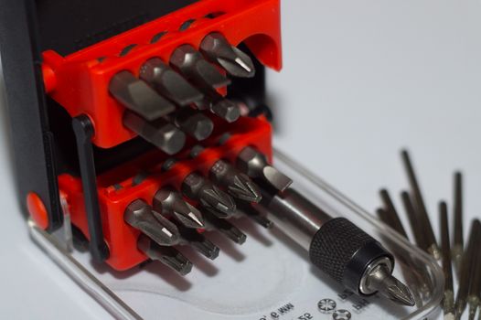 Bits holder in box and many tool bits on white background. Close-up view. Red element in plastic box.