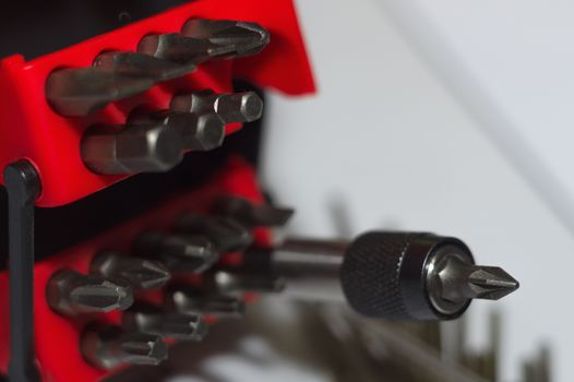 Bits holder in box and many tool bits on white background. Close-up view. Red element in plastic box.