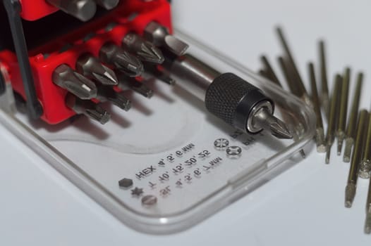 Bits holder in box and many tool bits on white background. Close-up view. Red element in plastic box.