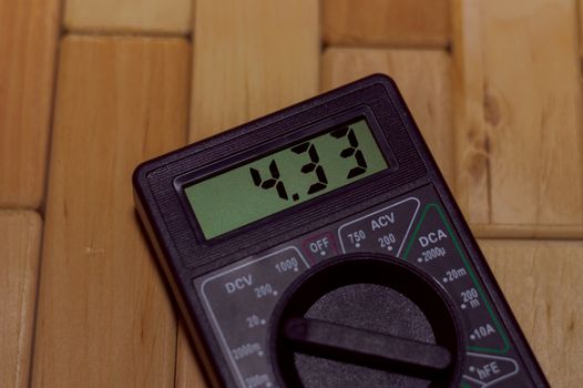Digital measuring multimeter on wooden floor. It shows 4.33V or fully charged battery. Includes voltmeter, ampermeter, ohmmeter.