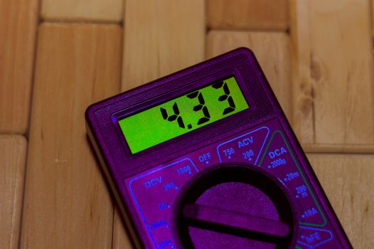 Purple digital measuring multimeter on wooden floor. It shows 4.33V on green screen or fully charged battery. Includes voltmeter, ampermeter, ohmmeter.