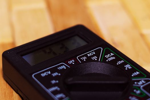 Digital measuring multimeter on wooden floor. It shows 4.33V or fully charged battery. Includes voltmeter, ampermeter, ohmmeter.