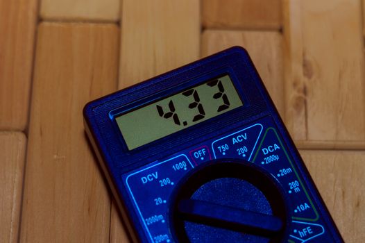 Blue digital measuring multimeter on wooden floor. It shows 4.33V or fully charged battery. Includes voltmeter, ampermeter, ohmmeter.