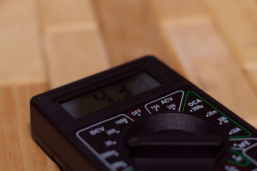 Digital measuring multimeter on wooden floor. It shows 4.33V or fully charged battery. Includes voltmeter, ampermeter, ohmmeter.