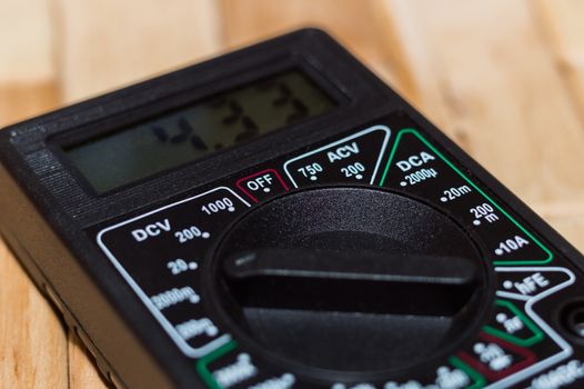 Digital measuring multimeter on wooden floor. It shows 4.33V or fully charged battery. Includes voltmeter, ampermeter, ohmmeter.