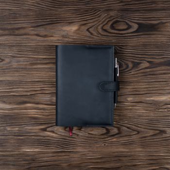 Black handmade leather notebook cover with notebook and pen on wooden background. Stock photo of luxury business accessories. Up to down view.