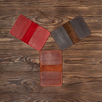 Tree handmade different colour leather cardholders on wooden background. Stock flat lay photo. Red, ginger and brown cardholders on photo.