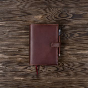 Brown handmade leather notebook cover with notebook and pen on wooden background. Stock photo of luxury business accessories. Up to down view.